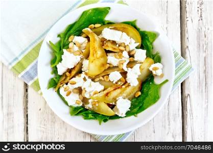 Salad of fried pear, spinach, salted feta cheese and cedar nuts in a plate on a napkin on a wooden board background from above