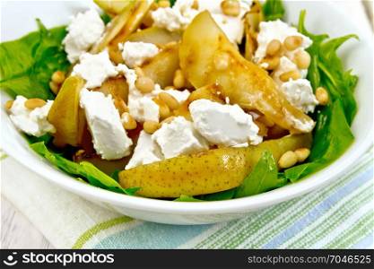 Salad of fried pear, spinach, salted feta cheese and cedar nuts in a plate on a towel against a light wooden board