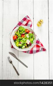 Salad of greens and tomatoes with olive oil. On a white wooden background.. Salad of greens and tomatoes with olive oil.