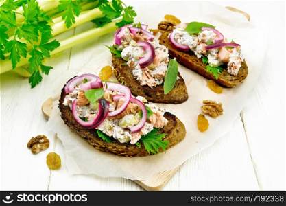 Salad of salmon, petiole celery, raisins, walnuts, red onions and cottage cheese on toasted bread with green lettuce on paper on a light wooden board background