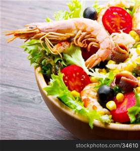 salad of shrimp, mixed greens, black olives anchovies and tomatoes on wooden background