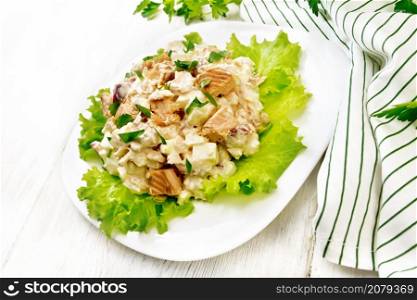 Salad of smoked salmon, cucumber, eggs and sweet pepper seasoned with sour cream on lettuce leaves in a plate, napkin, parsley on wooden board background