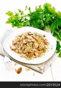 Salad of smoked salmon, rice, sunflower and pumpkin seeds, almonds, seasoned with honey and olive oil in a plate on towel, parsley and fork on background of light wooden board