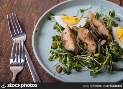 salad of sprouts and mackerel in a beautiful plate on a wooden background and next to two forks. Norwegian traditional cuisine