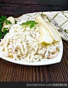Salad of squid, rice, pears and eggs in a plate, parsley, napkin and fork on a dark wooden board