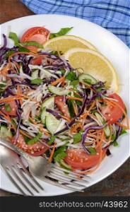 Salad of white and blue chopped cabbage, carrots, cucumber, tomato dressed with oil, lemon, sesame