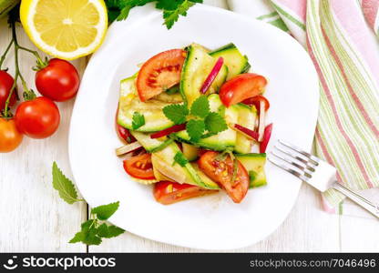 Salad of young zucchini, radish, tomato and mint, seasoned with lemon juice and soy sauce in a plate, napkin on a wooden board background from above