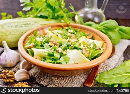 Salad of young zucchini, sorrel, garlic and nuts, seasoned with vegetable oil in a plate on napkin of sackcloth on a wooden board background