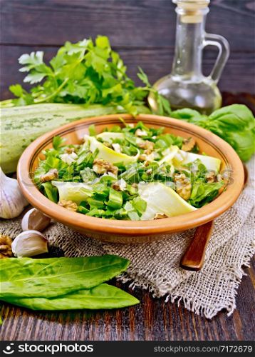 Salad of young zucchini, sorrel, garlic and nuts, seasoned with vegetable oil in clay plate on napkin of sackcloth on a dark wooden board background