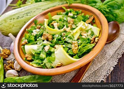 Salad of young zucchini, sorrel, garlic and walnuts, seasoned with vegetable oil in a plate on napkin of sackcloth on a background of dark wooden board. Salad with squash and sorrel on board