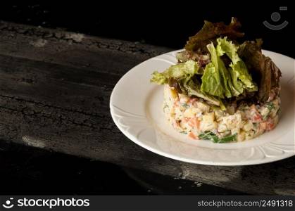 salad olivier in a white plate on a wooden old surface. Olivier salad with greens in a round plate on a wooden old board. dish on a wooden surface