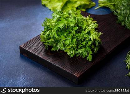 Salad, parsley and dill on a dark cutting board against a blue concrete background. Cooking a vegetarian dish with fresh greens. Salad, parsley and dill on a dark cutting board against a blue concrete background