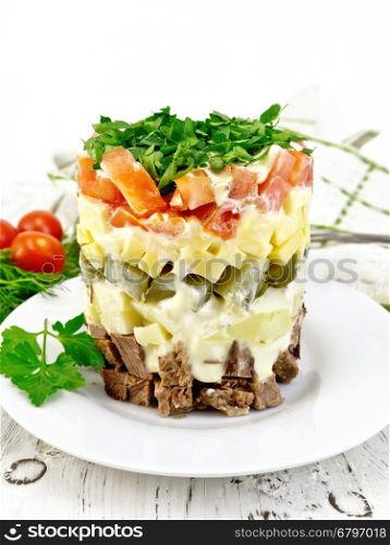 Salad with beef, boiled potatoes, pickles, cheese, tomato, parsley in a white plate, napkin, background dill on a wooden board