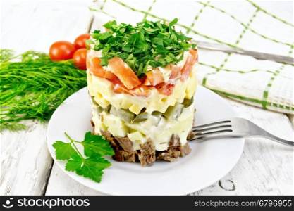 Salad with beef, boiled potatoes, pickles, cheese, tomato, parsley in the plate, napkin, dill on the background light wooden boards