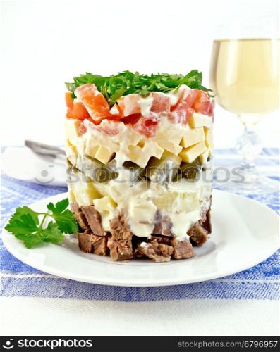 Salad with beef, boiled potatoes, pickles, cheese, tomato, parsley in the plate, glass of white wine on a background of blue linen tablecloth
