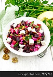Salad with beetroot, feta cheese, apple, walnuts, parsley, seasoned with balsamic vinegar and olive oil in a plate, green napkin against the background of a light wooden board