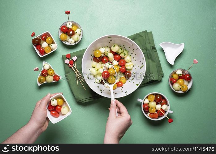 Salad with cherry tomatoes and mozzarella balls on green background. Above view of woman serving caprese salad. Summer salad portions. Healthy eating.