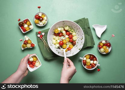 Salad with cherry tomatoes and mozzarella balls on green background. Above view of woman serving caprese salad. Summer salad portions. Healthy eating.