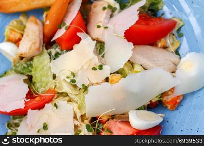 Salad with chicken and fresh vegetables. Fresh salad of chicken with vegetables and cheese, on a blue background