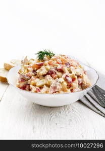 Salad with chicken, sweet pepper, tomato, egg and cheese seasoned with mayonnaise and garlic in a dish, towel, bread and forks on a white wooden board background