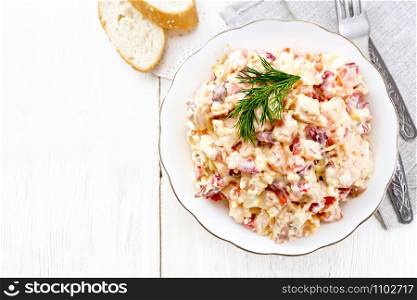 Salad with chicken, sweet pepper, tomato, egg and cheese seasoned with mayonnaise and garlic in a dish, towel, bread and forks on a light wooden board from above