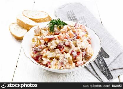 Salad with chicken, sweet pepper, tomato, egg and cheese seasoned with mayonnaise and garlic in a dish, towel, bread and forks on a light wooden board background