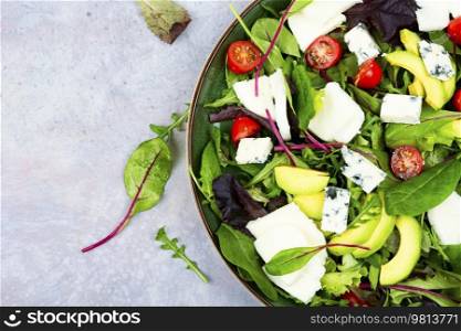 Salad with fresh lettuce, greens, avocado, tomatoes and cheeses. Top view. Copy space. Fresh vegetable salad with greens and mozzarella