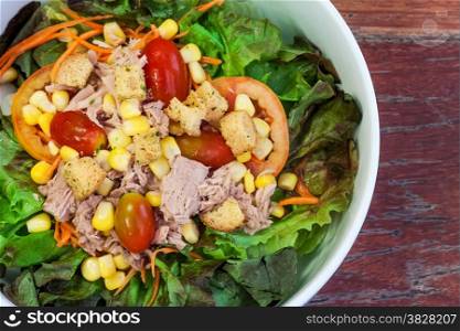 Salad with fresh tuna in white bowl on brown wooden background