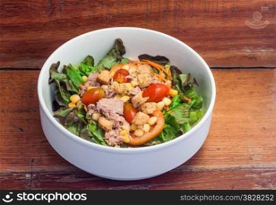 Salad with fresh tuna in white bowl on brown wooden background
