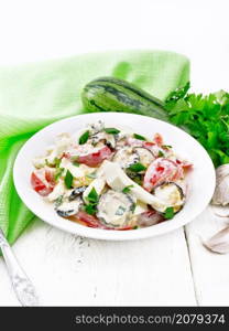 Salad with fried zucchini, boiled egg, fresh tomato and garlic, dressed with mayonnaise or sour cream in a plate, napkin and parsley on the background of light wooden board