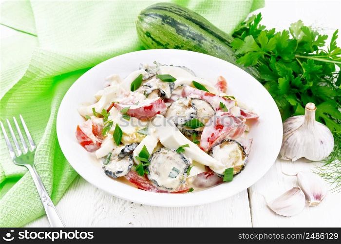 Salad with fried zucchini, boiled egg, fresh tomato and garlic, dressed with mayonnaise in plate, napkin and parsley on white wooden board background
