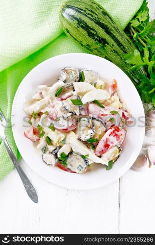 Salad with fried zucchini, boiled egg, fresh tomato and garlic, seasoned with mayonnaise or sour cream in a plate, towel and parsley on wooden board background from above