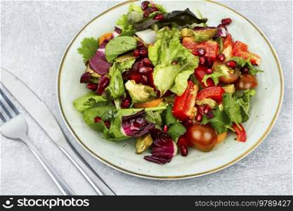 Salad with greens, pepper, red lettuce and cucumber, decorated with pomegranate. Healthy food concept.. Spring bright vegetable salad.