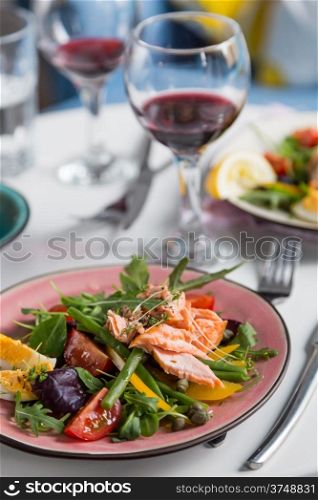 salad with salmon and verdure in pink plate on table with blue chair background