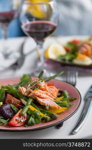 salad with salmon and verdure in pink plate on table with blue chair background