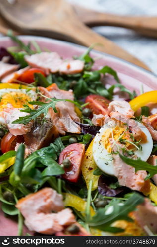 salad with salmon, vegetables and verdure in pink plate on retro newspaper background