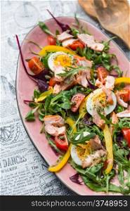 salad with salmon, vegetables and verdure in pink plate on retro newspaper background