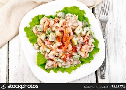 Salad with shrimp, avocado, tomatoes and mayonnaise on the green lettuce in the plate, napkin, fork on the background of the wooden planks on top