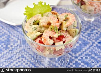 Salad with shrimp, avocado, tomatoes, green lettuce in a glass goblet, a plate against the background of blue linen tablecloth