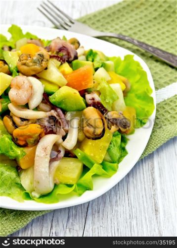 Salad with shrimp, octopus, mussels and calamari with avocado, lettuce and pineapple in a plate on a napkin on a light wooden board