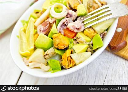 Salad with shrimp, octopus, mussels and calamari with avocado, lettuce, lemon and pineapple in a bowl on the background light wooden boards