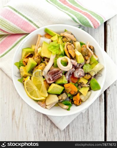 Salad with shrimps, octopus, mussels and calamari with avocado, lettuce, lemon and pineapple in a bowl on a napkin on the background light wooden boards