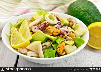 Salad with shrimps, octopus, mussels and calamari with avocado, lettuce, lemon and pineapple on a plate, napkin on the background light wooden boards