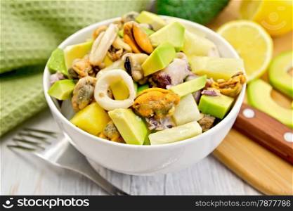 Salad with shrimps, octopus, mussels and calamari with avocado, lettuce, lemon and pineapple in a bowl, napkin on the background light wooden boards
