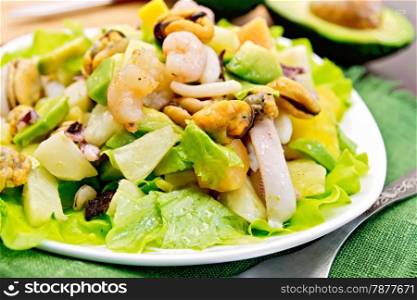 Salad with shrimps, octopus, mussels and calamari with avocado, lettuce, pineapple in plate on a green napkin, fork on the background dark wooden boards