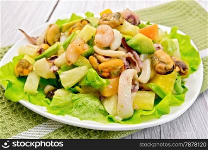 Salad with shrimps, octopus, mussels and calamari with avocado, lettuce, pineapple in plate on a green napkin on the background light wooden boards