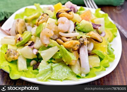 Salad with shrimps, octopus, mussels and calamari with avocado, lettuce, pineapple in plate, napkin, fork on the background dark wooden boards