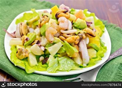 Salad with shrimps, octopus, mussels and calamari with avocado, lettuce, pineapple in a plate on a napkin, fork on the background dark wooden boards