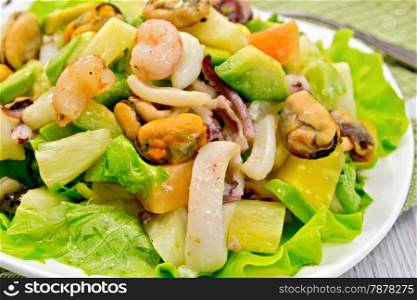 Salad with shrimps, octopus, mussels and calamari with avocado, lettuce, pineapple on a plate, fork, napkin on the background light wooden boards