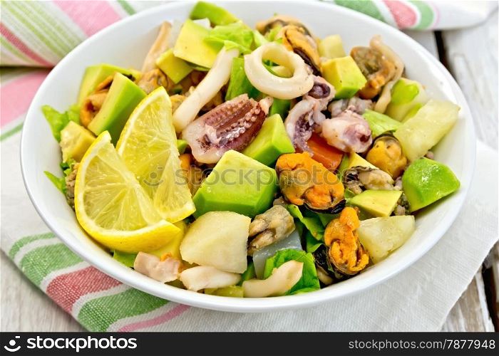 Salad with shrimps, octopus, mussels and squid, avocado, lettuce, lemon and pineapple in a bowl on a napkin on the background light wooden boards